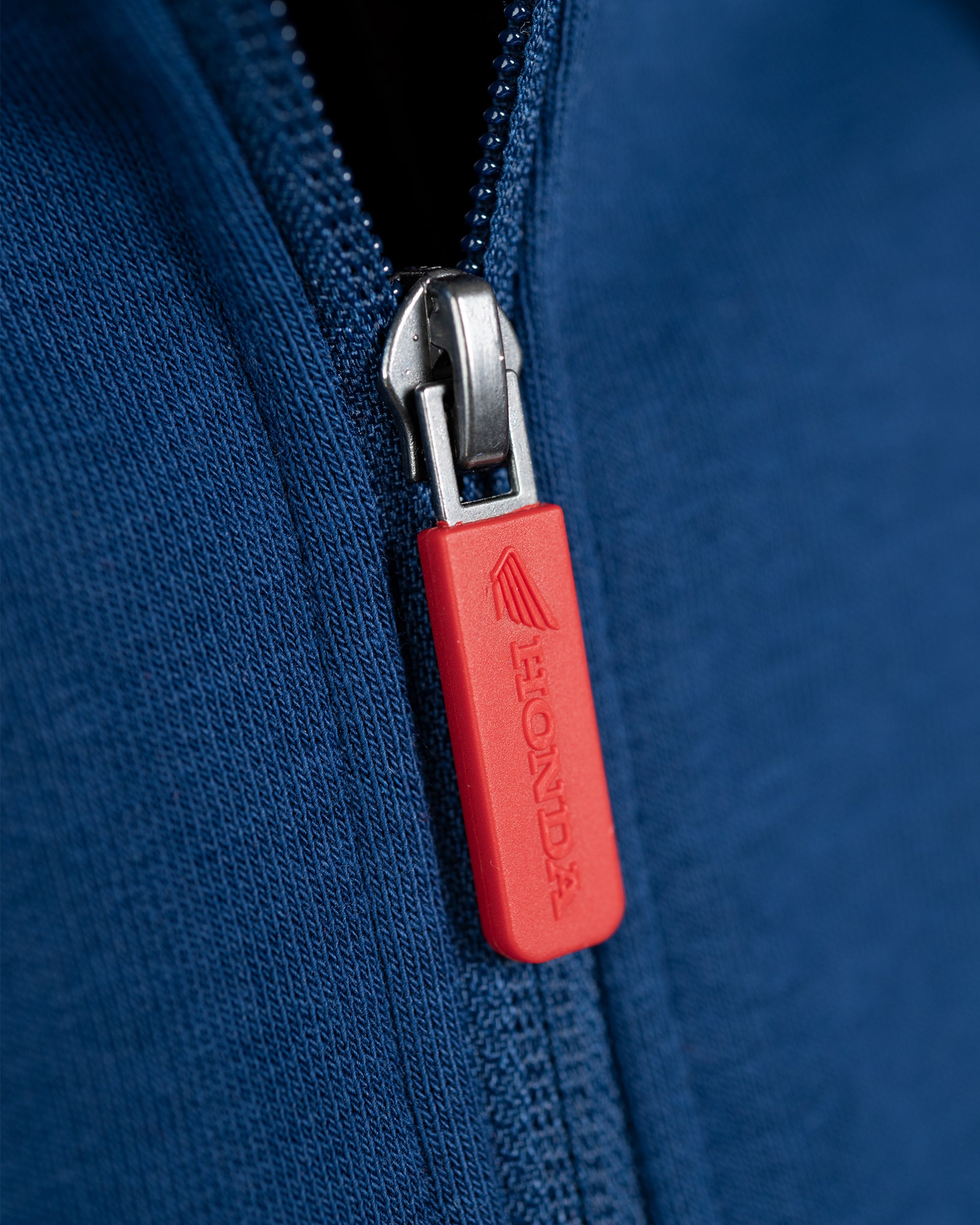 Roter Zipper-Anhänger mit geprägtem Honda Schriftzug am blauen Zip-Hoodie.
