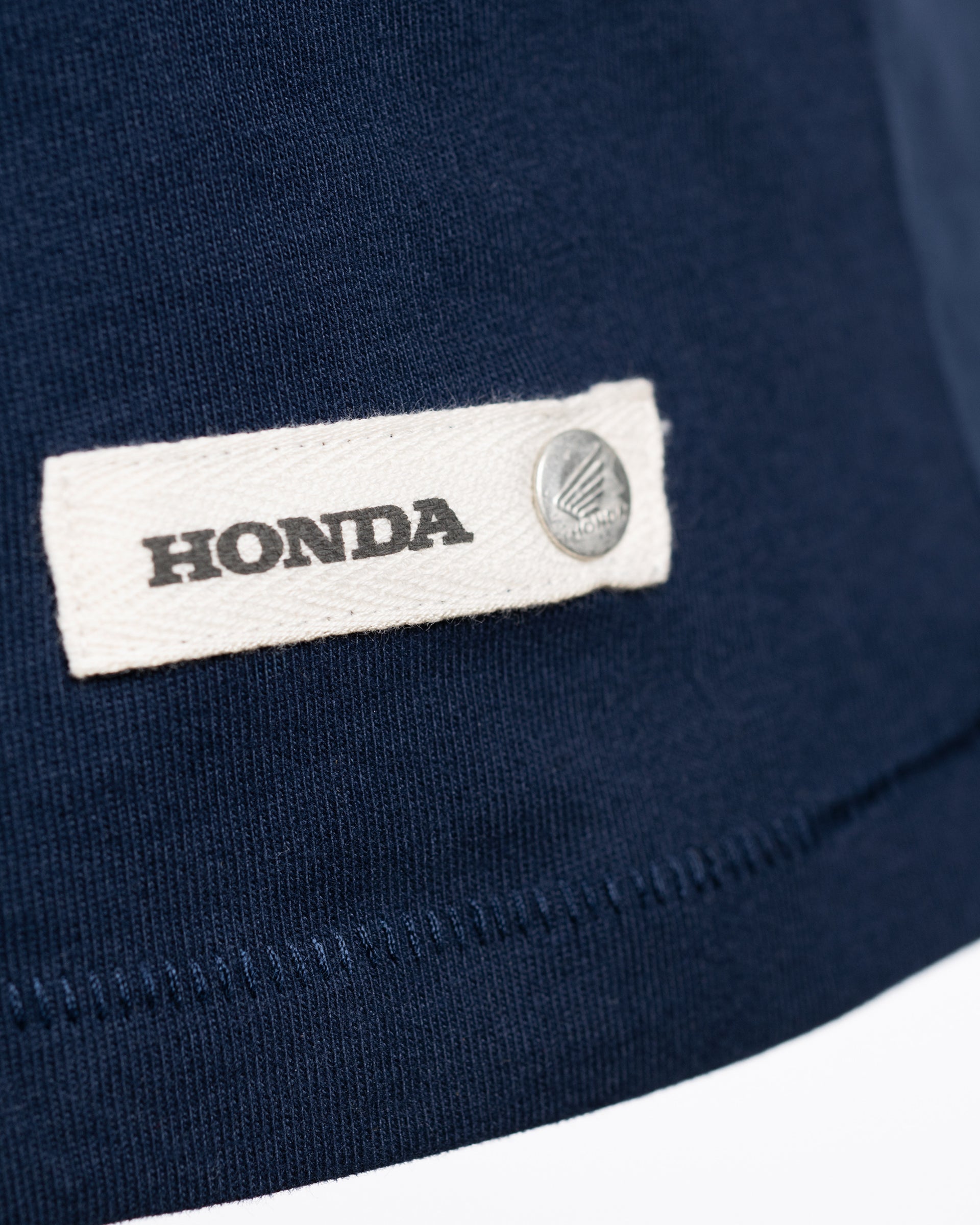 Honda Sunset T-Shirt Blau, Detailansicht Textiletikett mit Hondalogoaufdruck und silbernem Coin.
